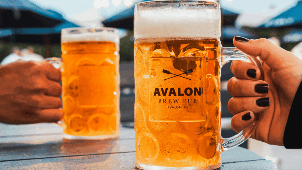 Closeup of two hands holding mugs of beer with the Avalon Brew Pub logo on them