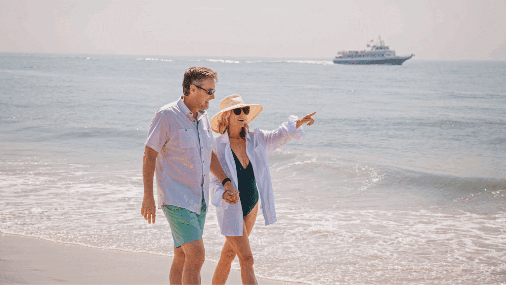 Couple on the beach along the ocean in their swimsuits pointing to something they see out of frame