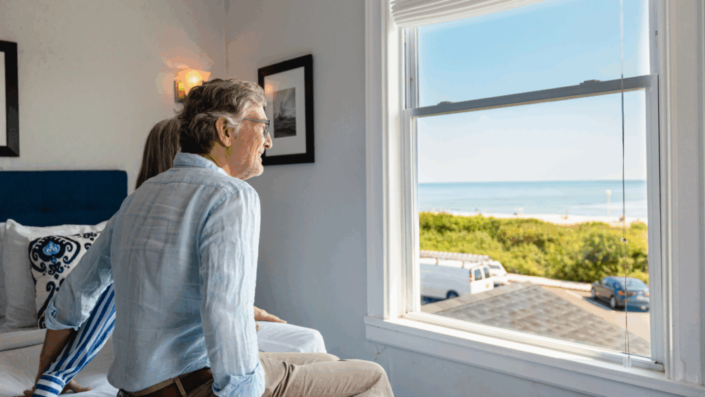 Couple sitting on the bed in their Grand Victorian hotel room in Spring Lake, NJ, looking out the window at an ocean view.