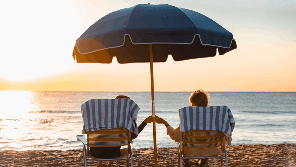 A couple on the beach in Spring Lake, NJ. They sit in beach chairs, holding hands under a beach umbrella while they take in the sunrise over the ocean.