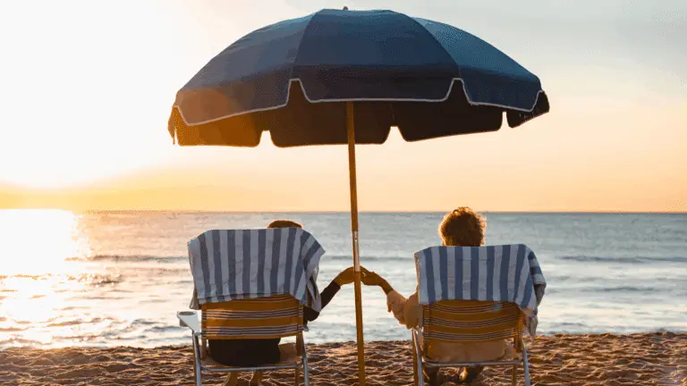 A couple on the beach in Spring Lake, NJ. They sit in beach chairs, holding hands under a beach umbrella while they take in the sunrise over the ocean.