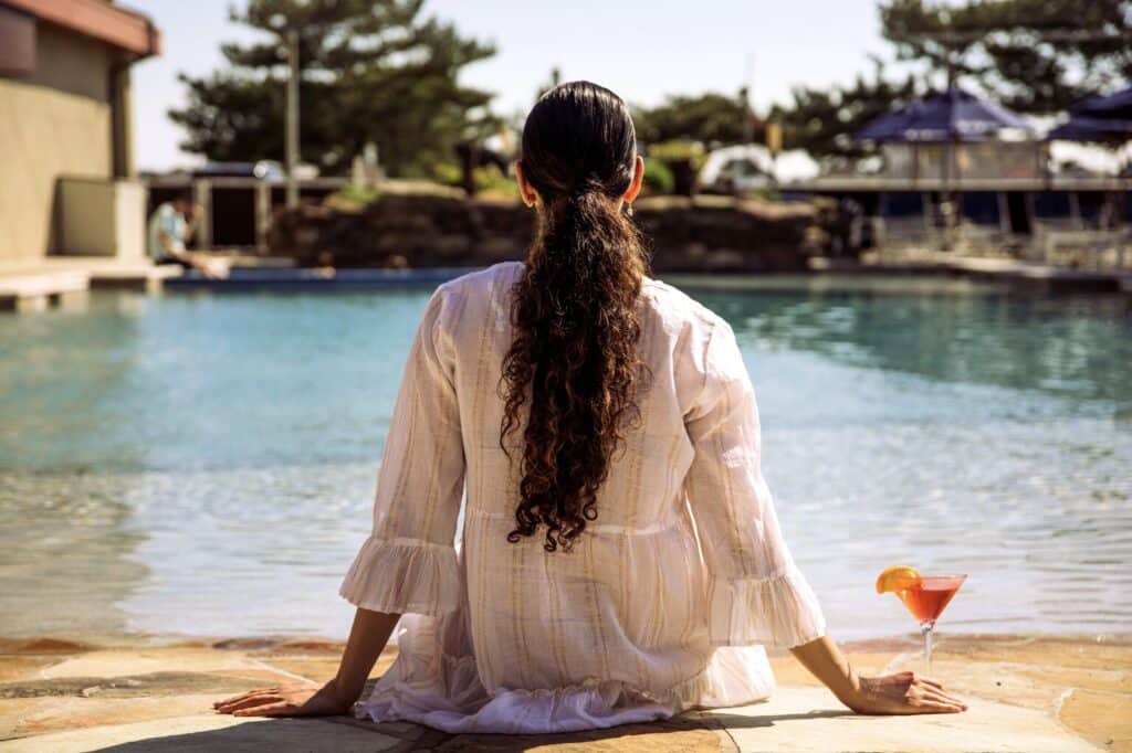 A woman sitting in front of the ICONA Windrift pool with a drink in her hand.